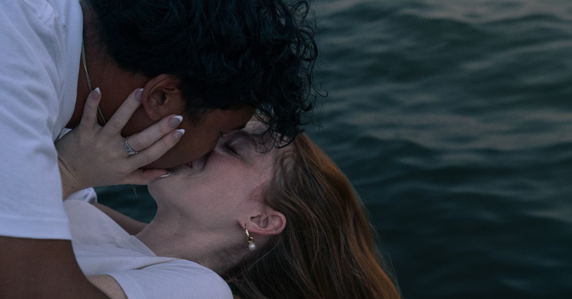 Close romantic kiss beside the water at dusk during a couples session