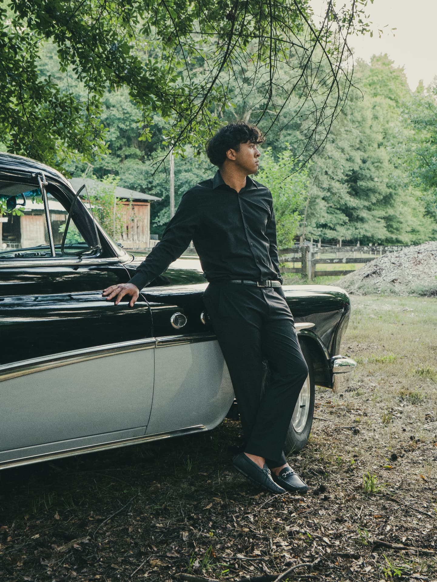 Man in black leaning against a vintage car under North Georgia trees
