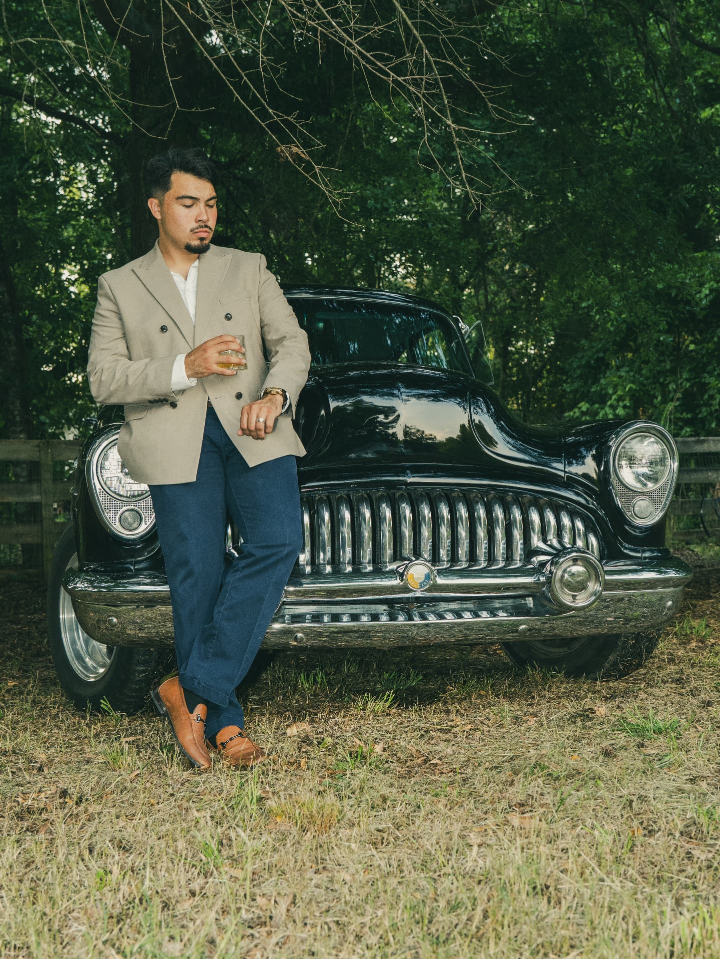 Man in a tan blazer leaning against a vintage black car on location in North Georgia