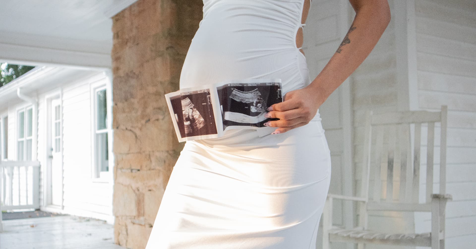 Maternity detail of a white gown and ultrasound photos in warm porch light