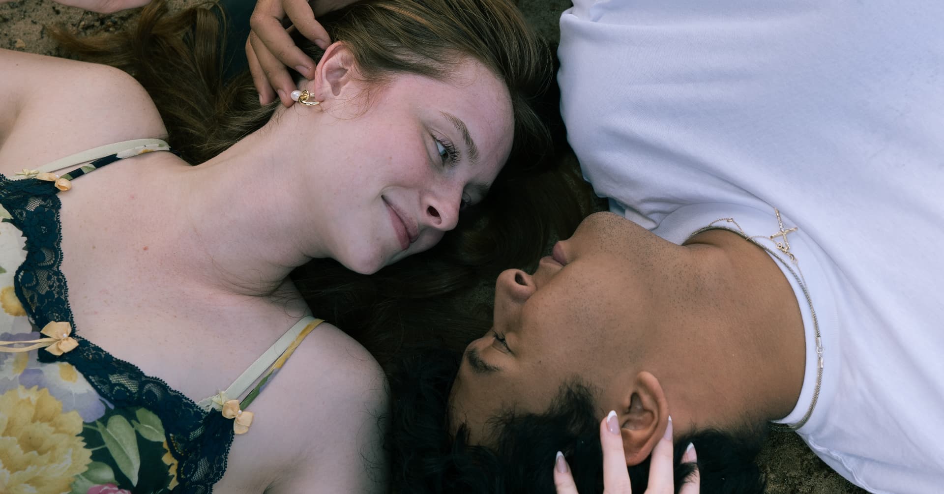 Couple lying side by side on the sand smiling at each other