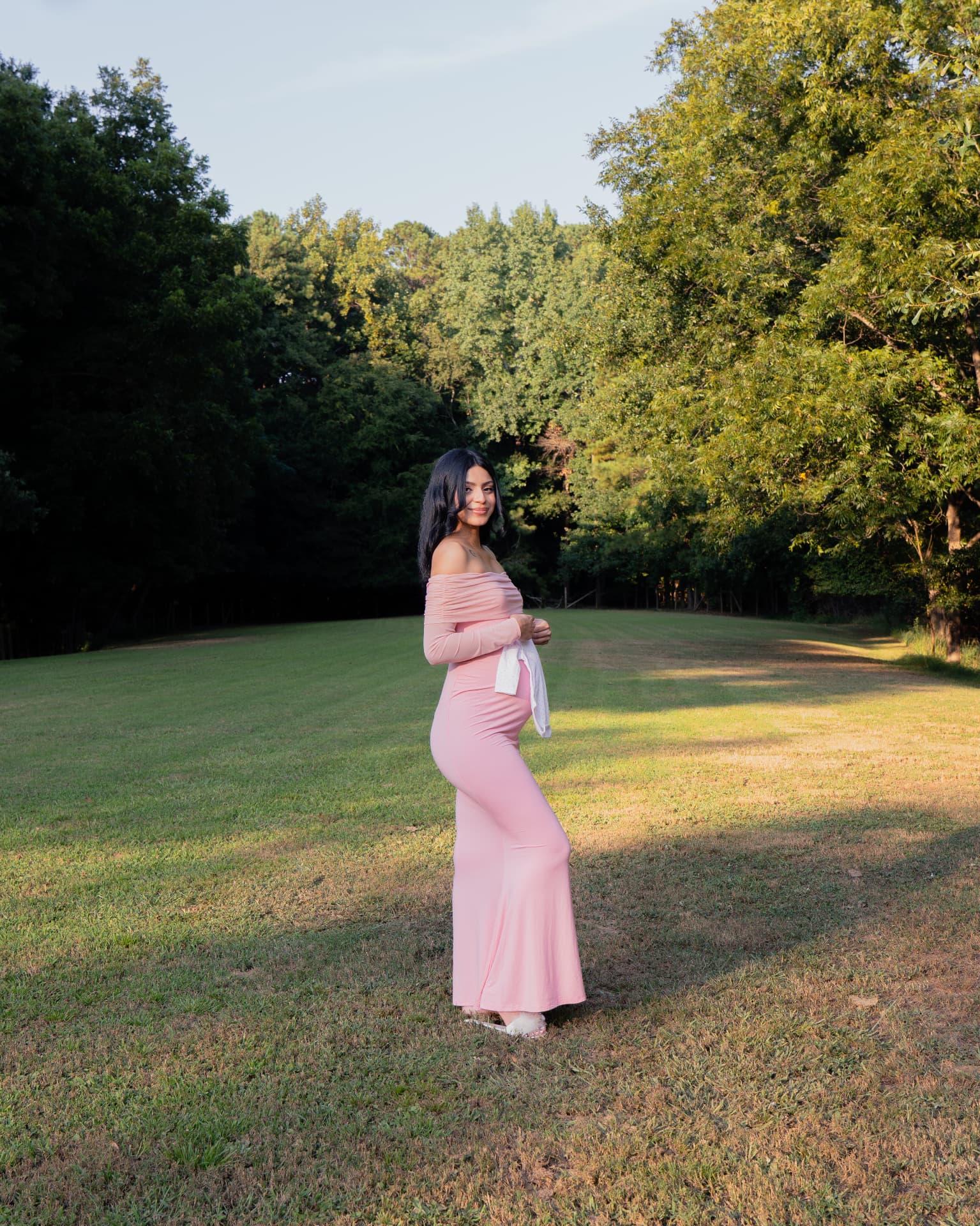 Expecting mother smiling in a pink gown on an open green field