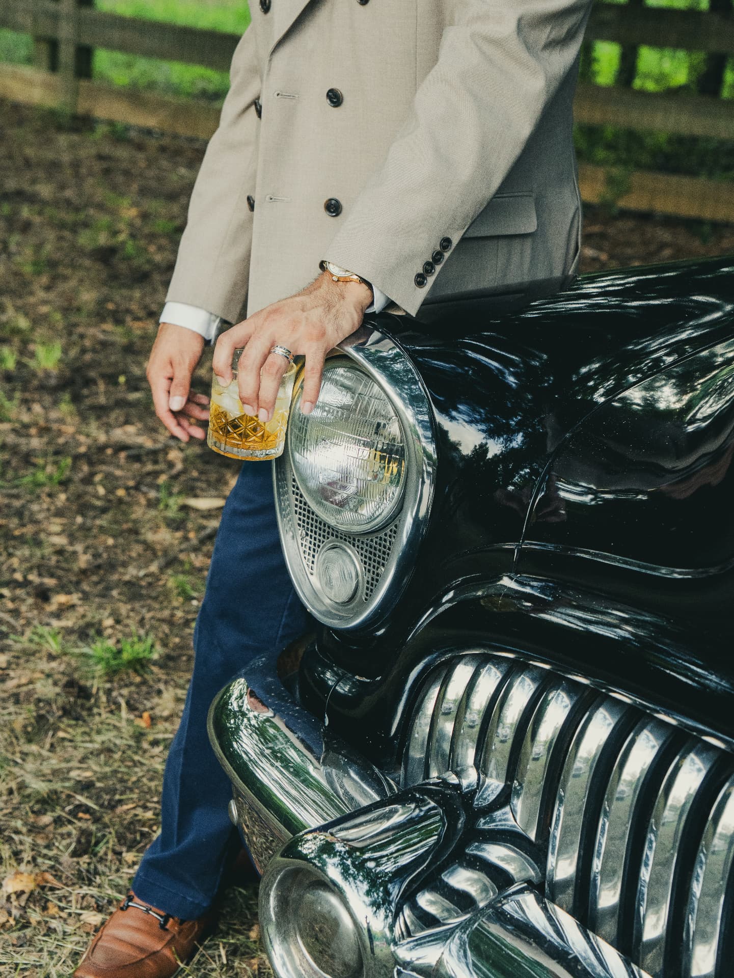 Man holding a whiskey glass beside a classic car grille