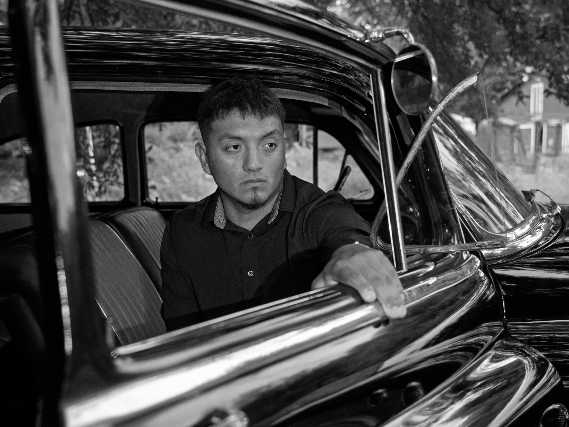 Black and white portrait of a man seated in a classic car