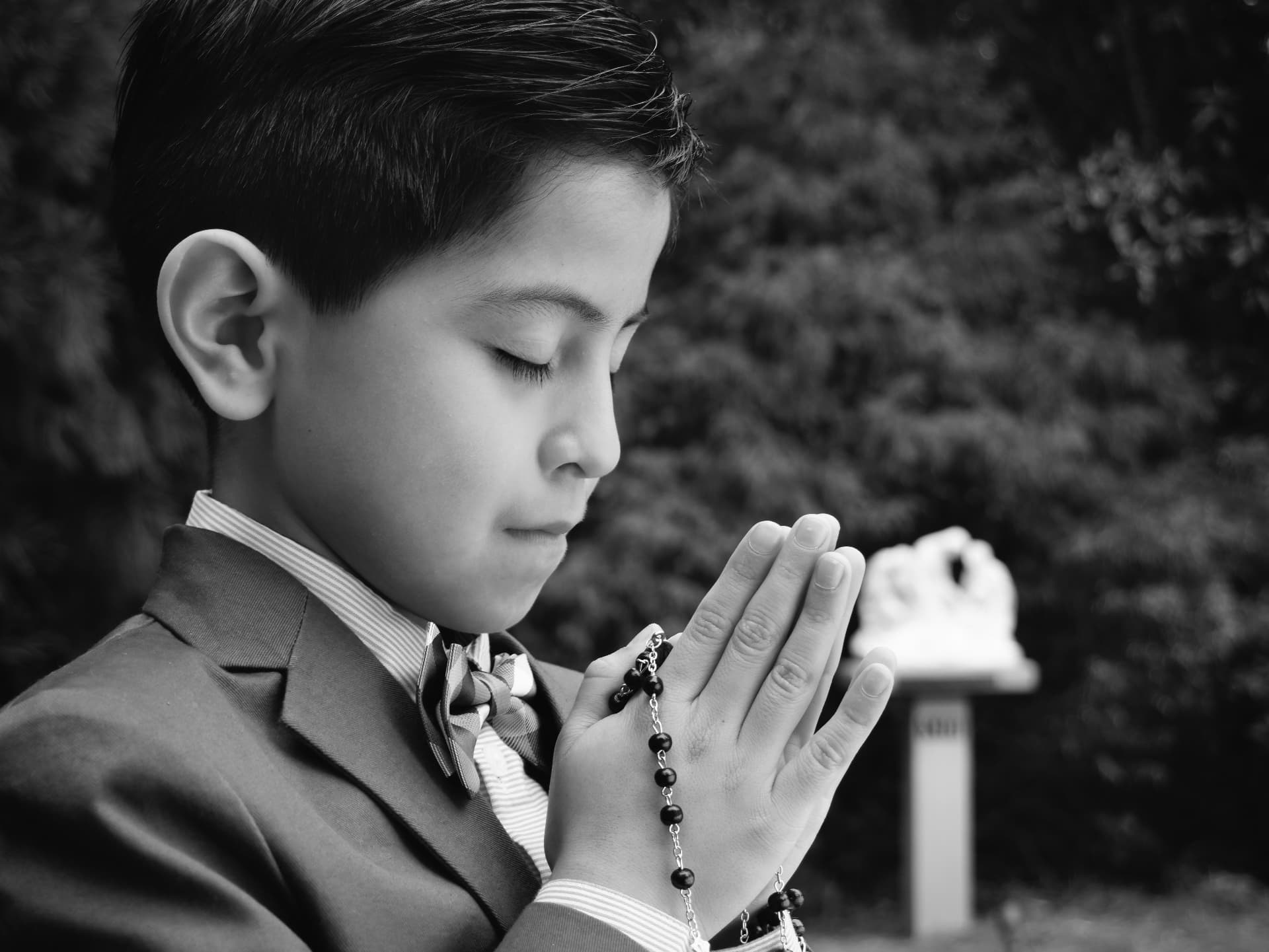 Black and white profile of a boy praying with a rosary