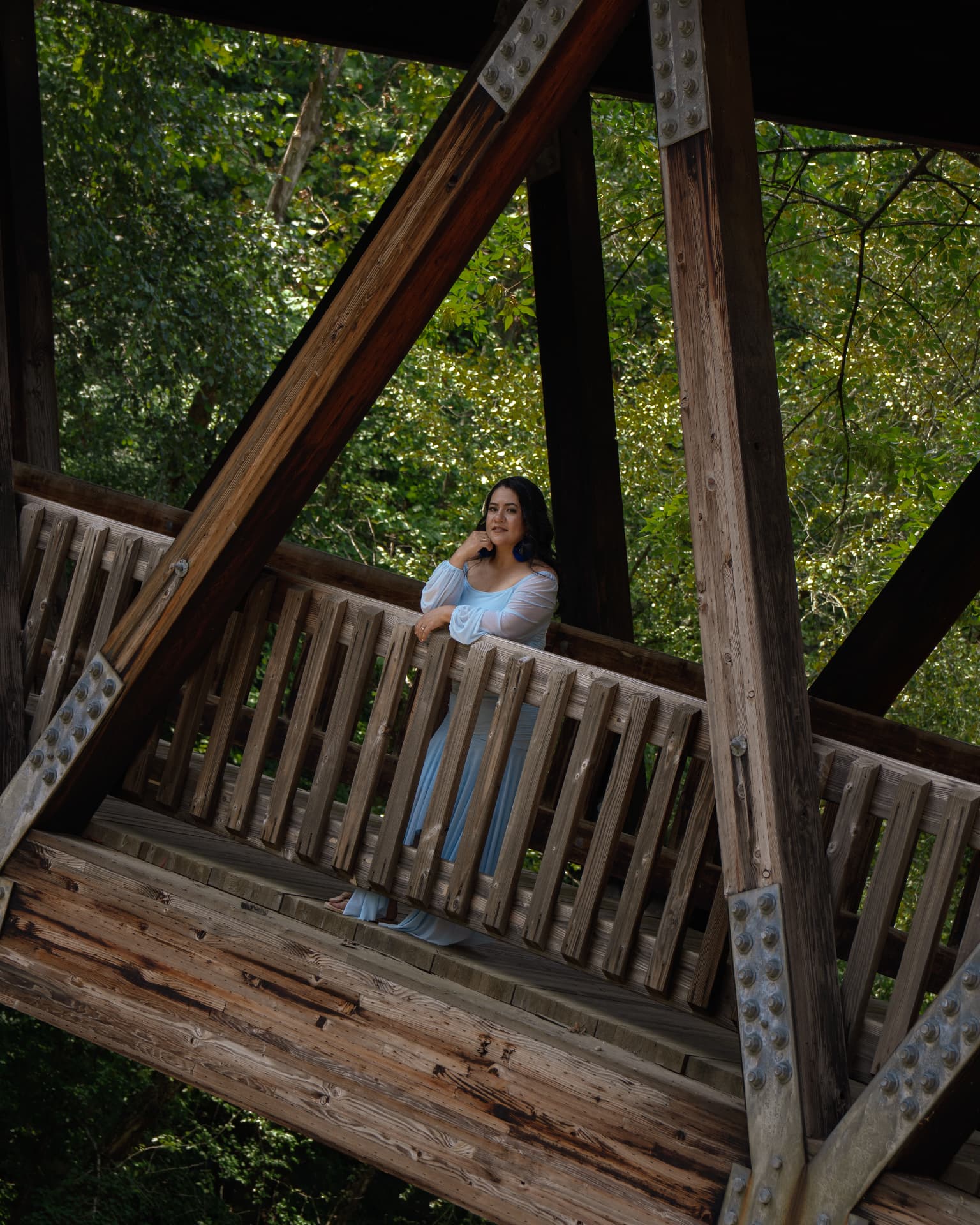 Woman in a light blue gown leaning on the rail of a covered wooden bridge in North Georgia