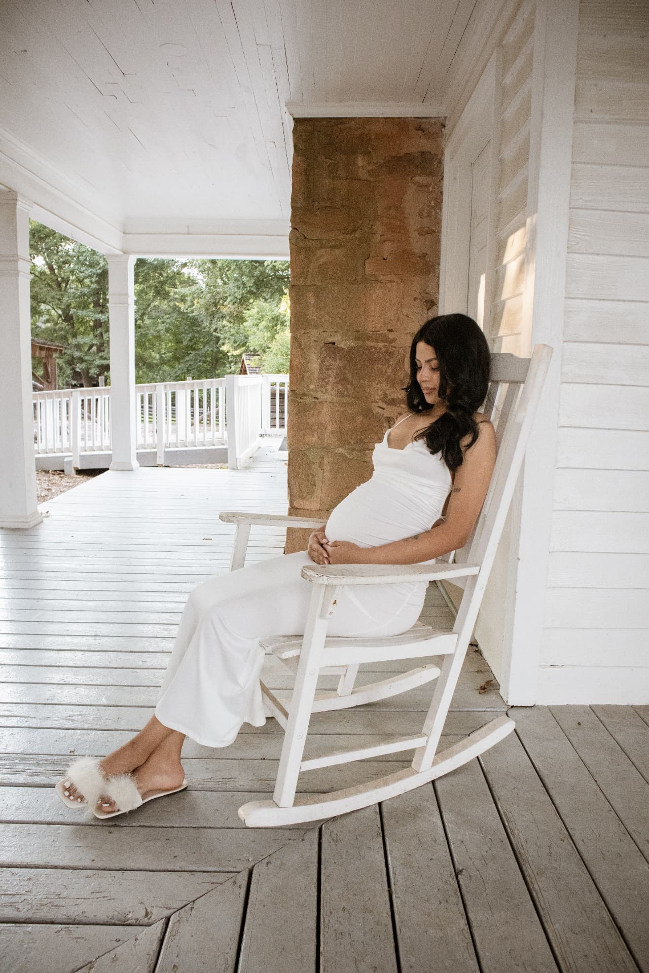 Expecting mother resting in a white rocking chair on a farmhouse porch