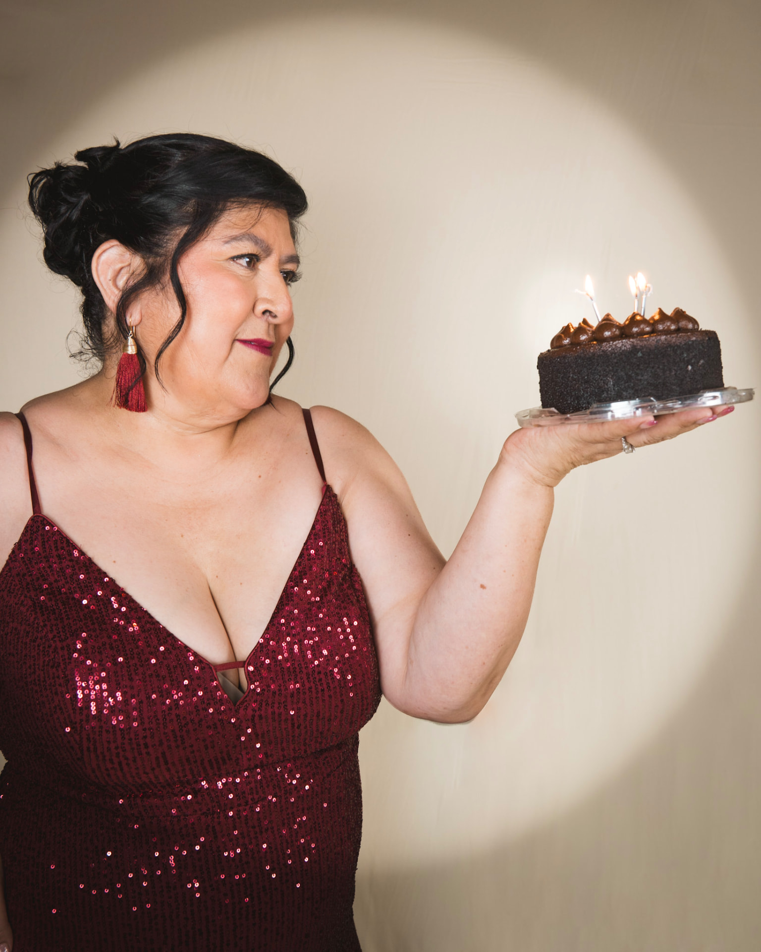 Woman in a sequin gown holding a chocolate birthday cake in studio