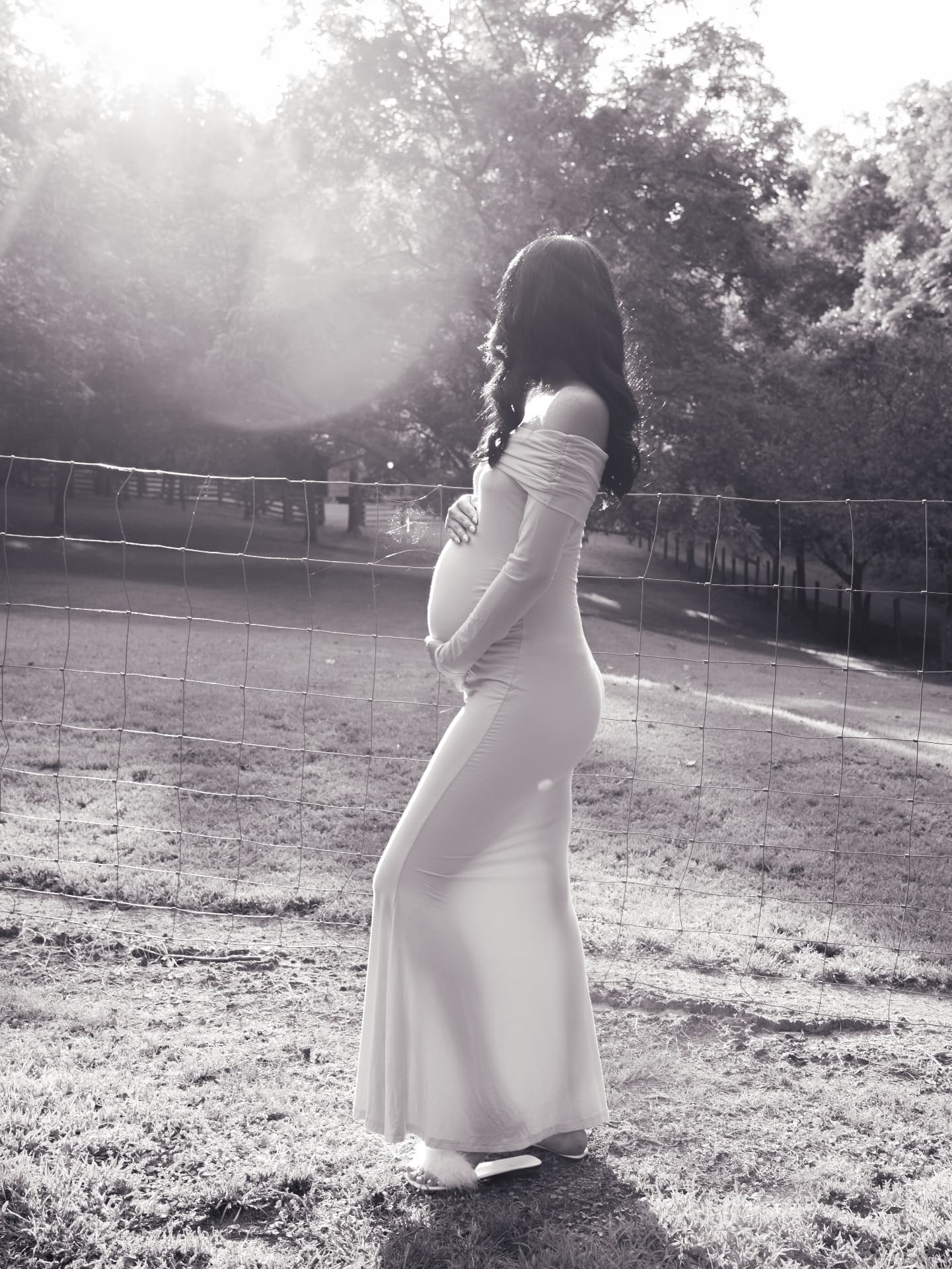 Black and white backlit maternity silhouette beside a country fence