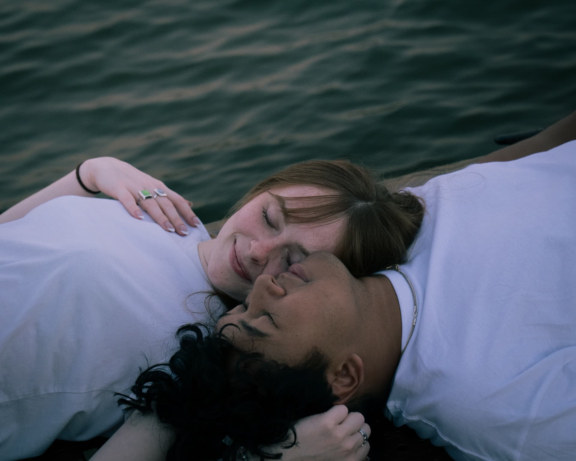Couple lying together on a dock resting cheek to cheek above the water