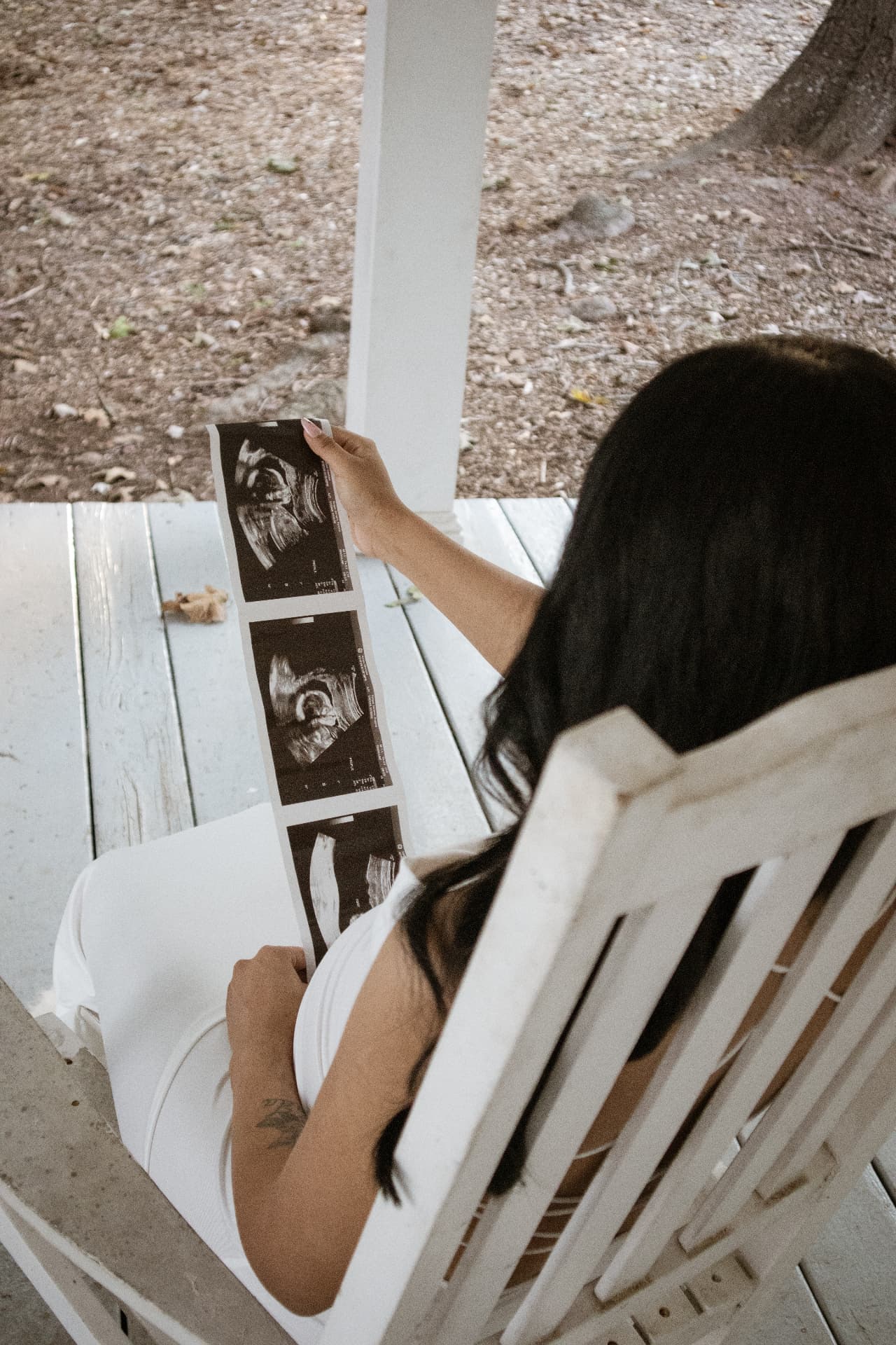 Mother-to-be looking at ultrasound photos while seated on a porch swing