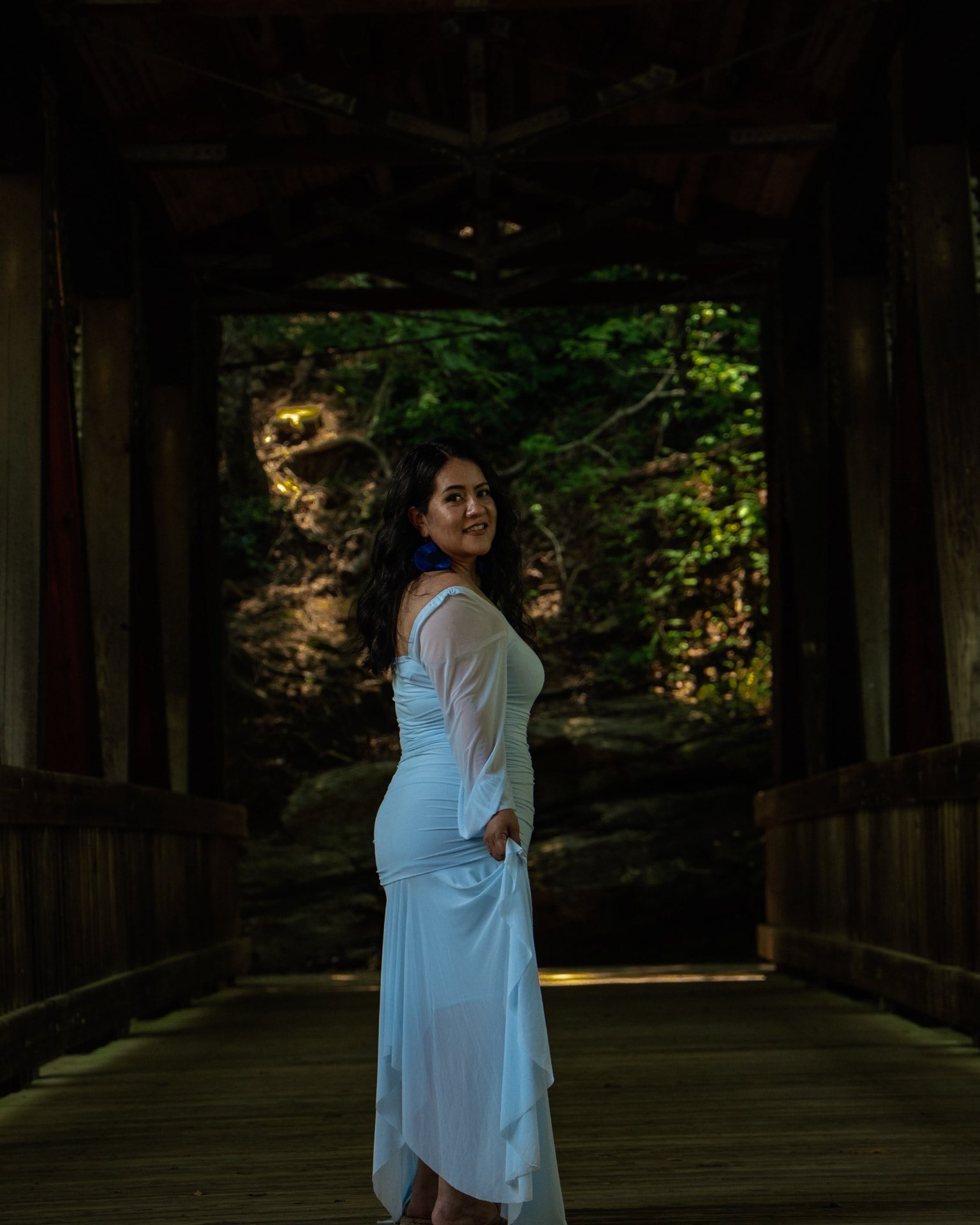 Woman in a blue gown turning toward the camera inside a covered bridge