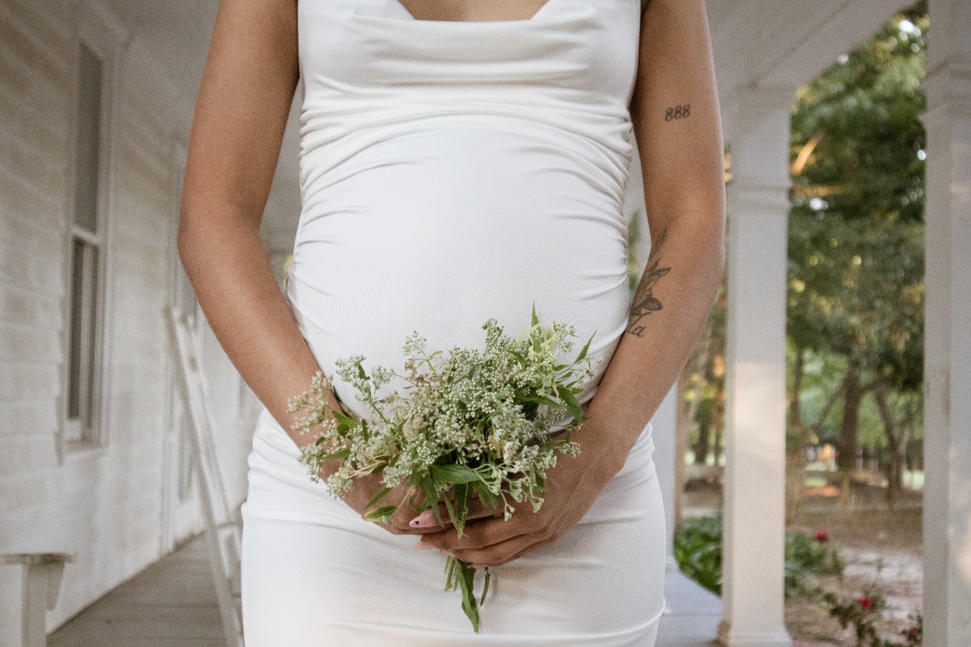 Close maternity detail of hands cradling the bump with a wildflower bouquet