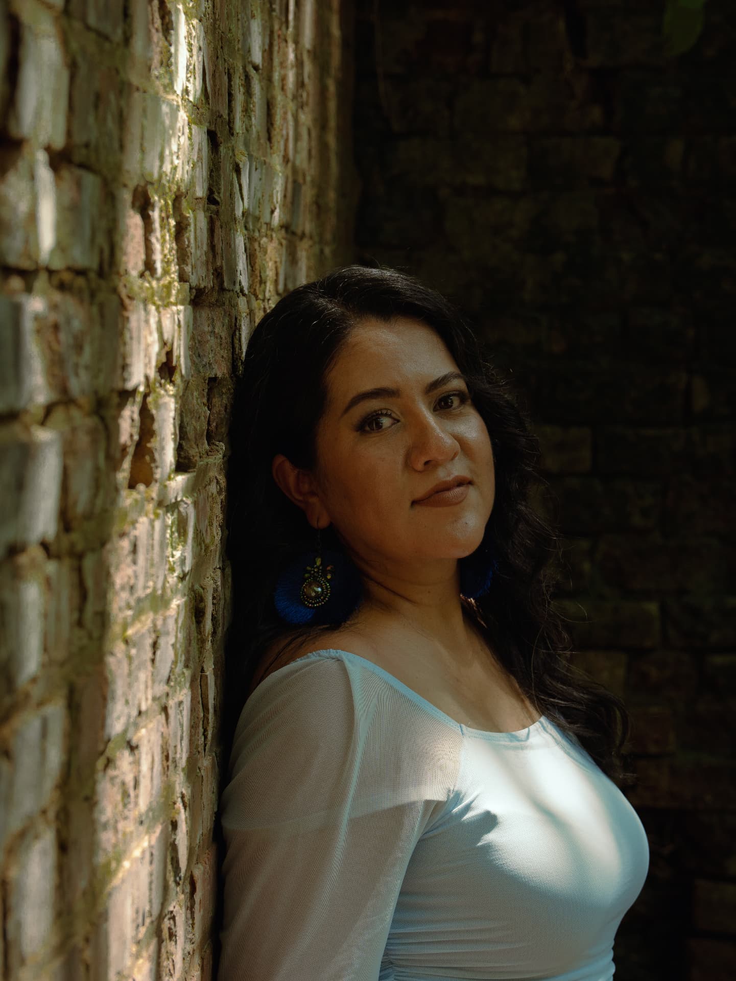 Portrait of a woman in a light blue top leaning against a sunlit brick wall in North Georgia