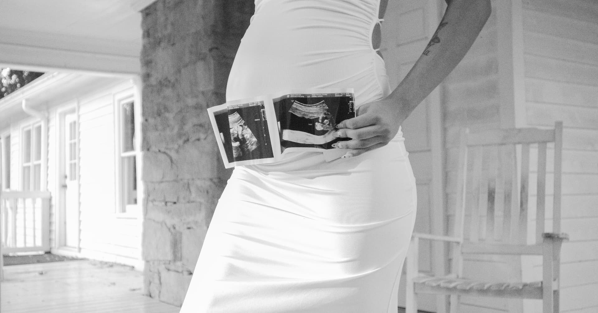 Black and white maternity detail of a bump with ultrasound photos on a porch