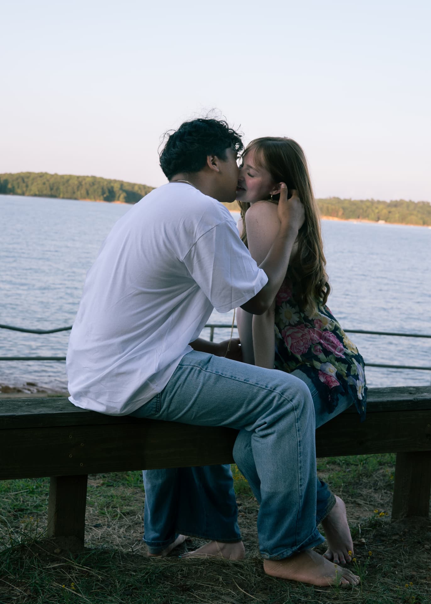 Couple sharing a kiss on a wooden bench overlooking the lake at sunset