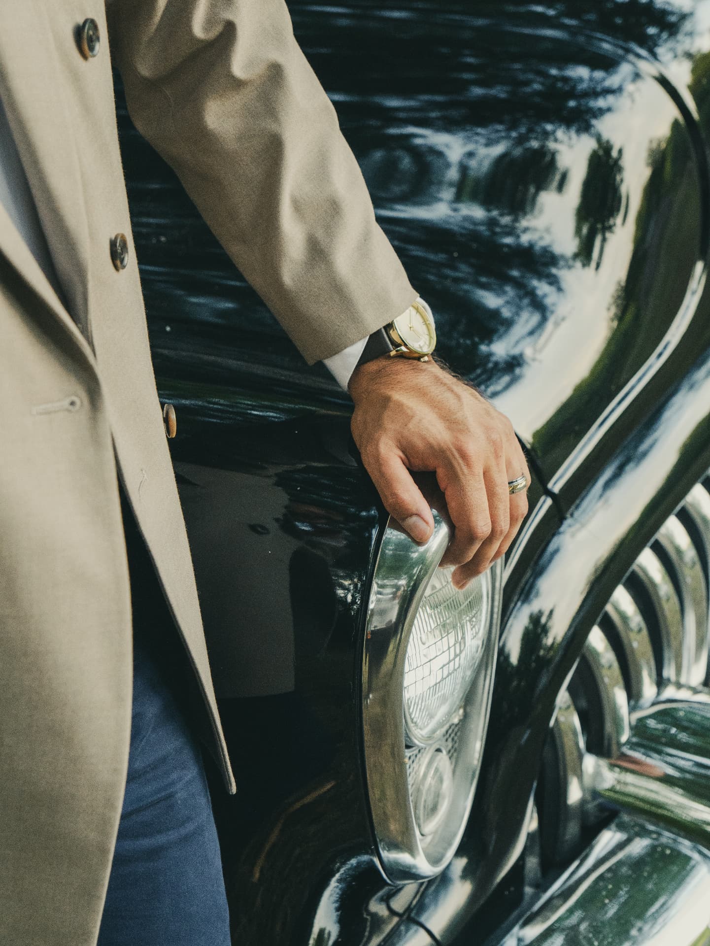 Detail of a hand with gold watch resting on a vintage car headlight