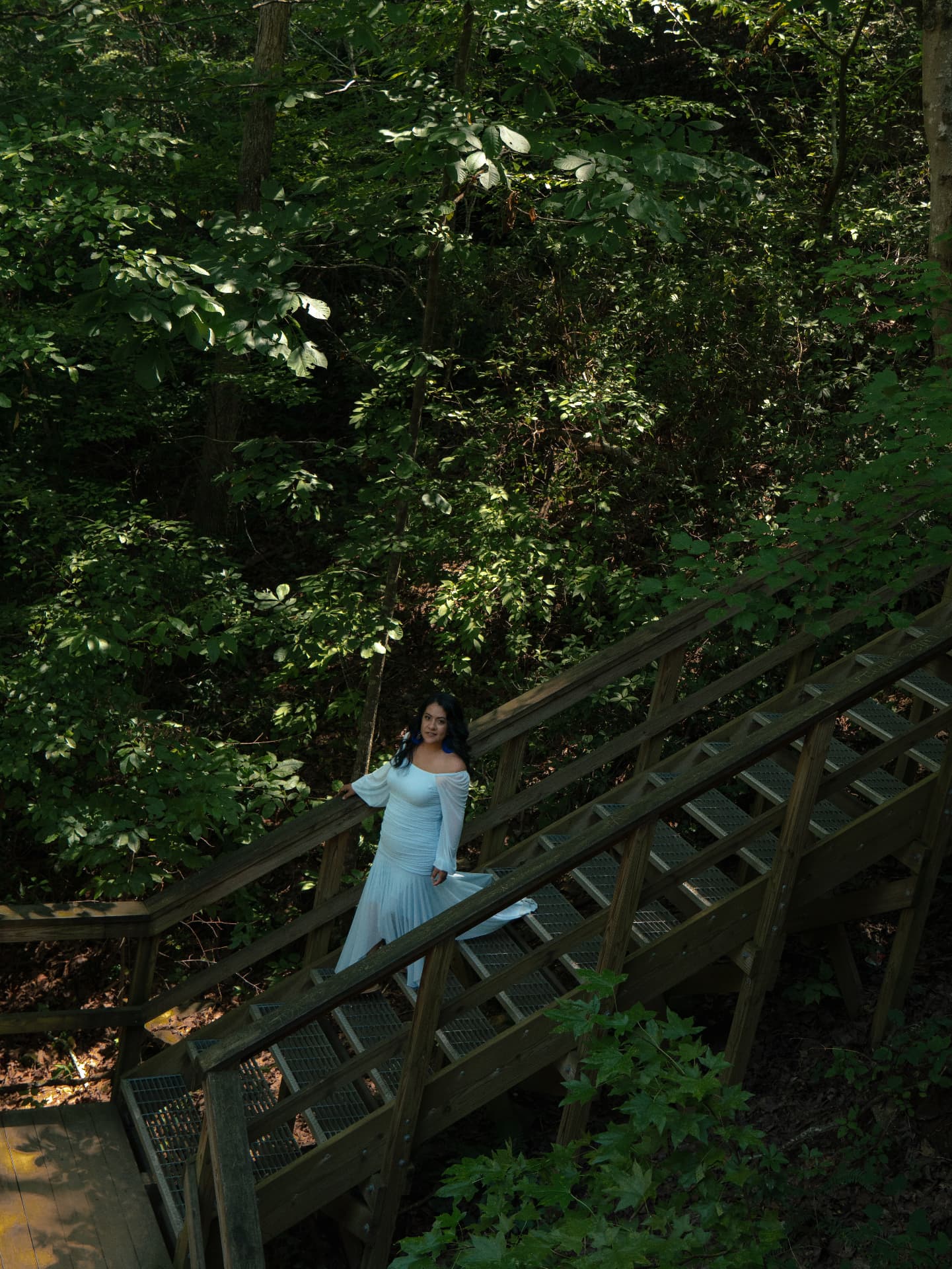 Woman in a blue gown on a wooden forest stairway surrounded by greenery