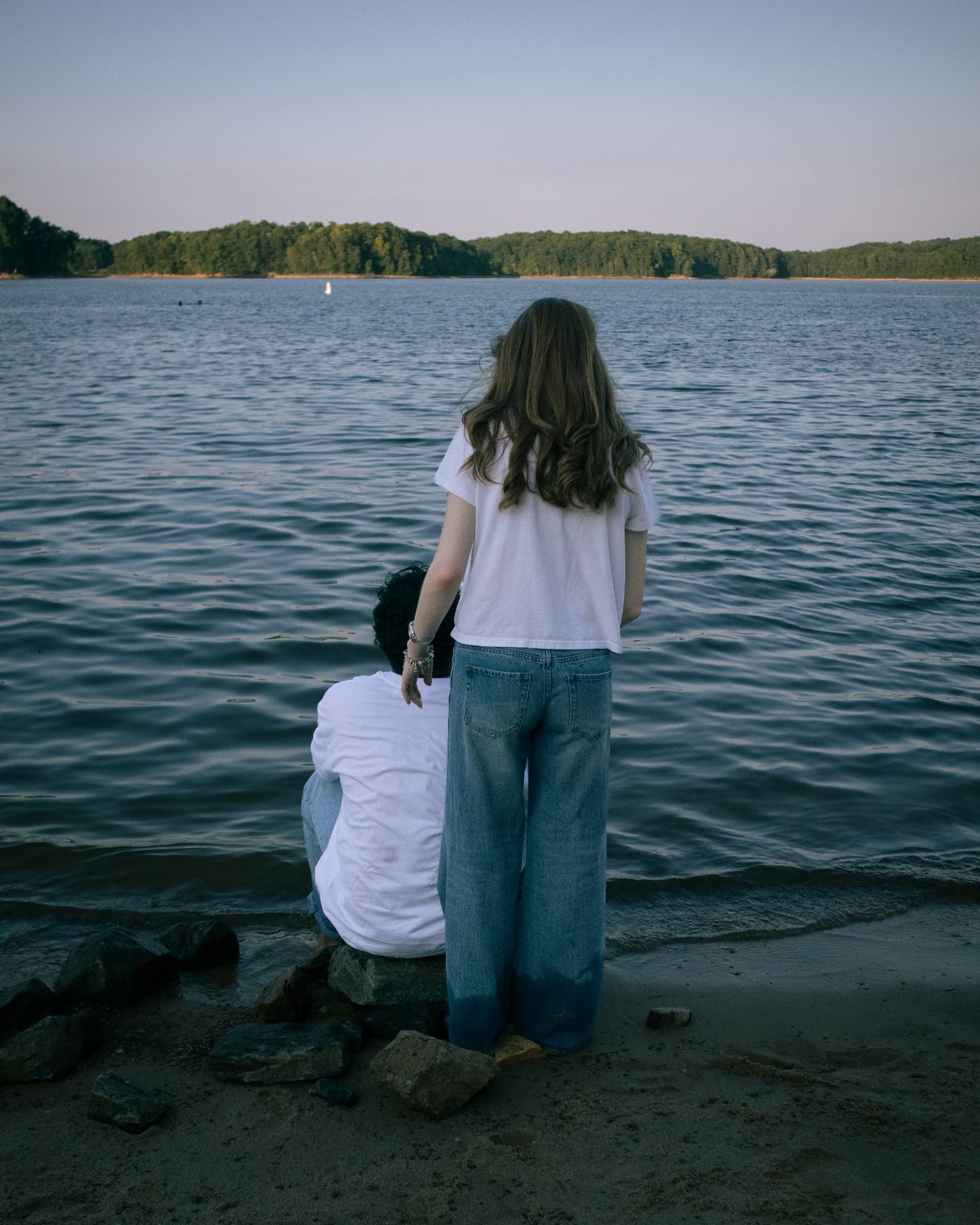 Couple resting at the shoreline as the sun sets over the lake
